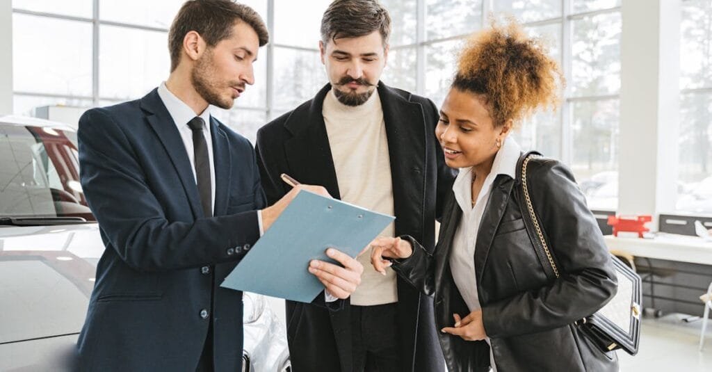 Three business professionals discussing car purchase details inside a modern dealership.
