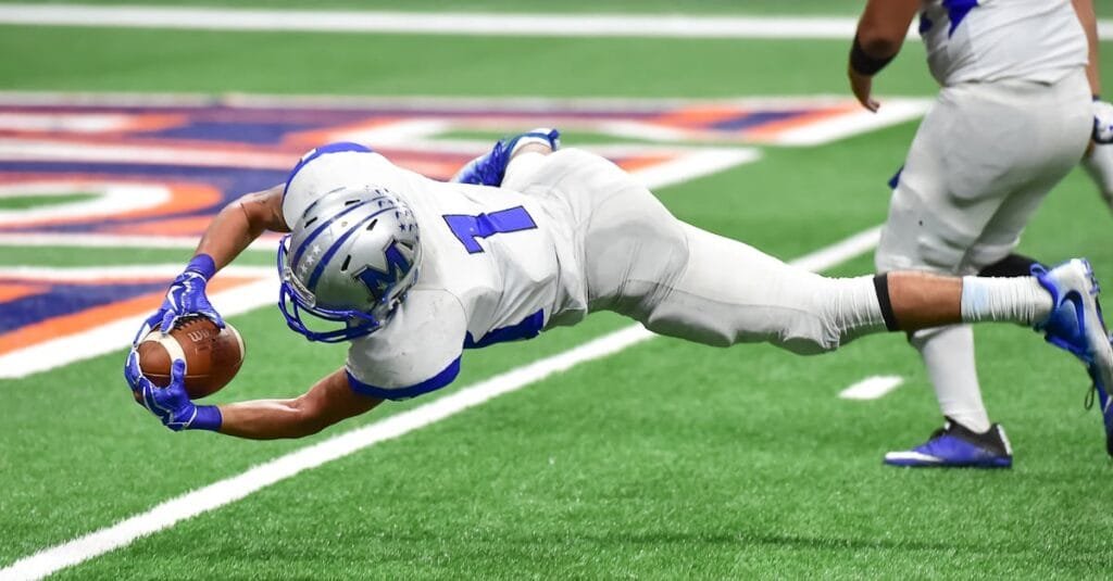 Football player making an incredible diving catch during a high-energy game in the stadium.