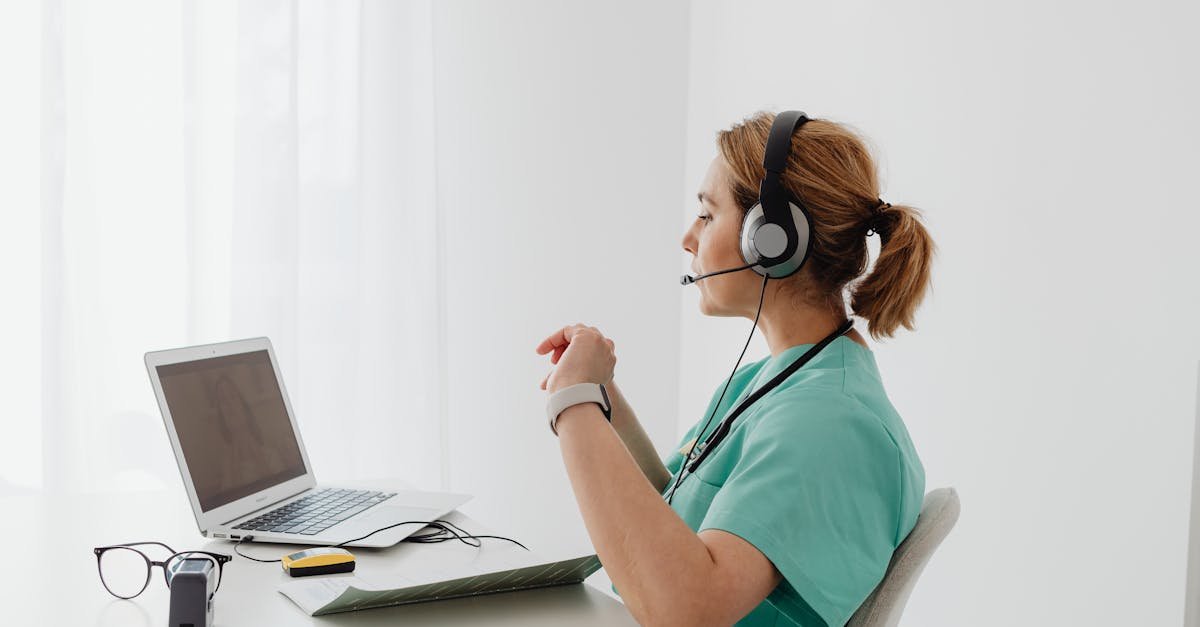 A female doctor using a laptop for an online consultation, wearing a headset in a bright office.