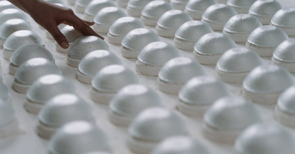 A person gently inspects rows of ceramic molds in a factory setting.