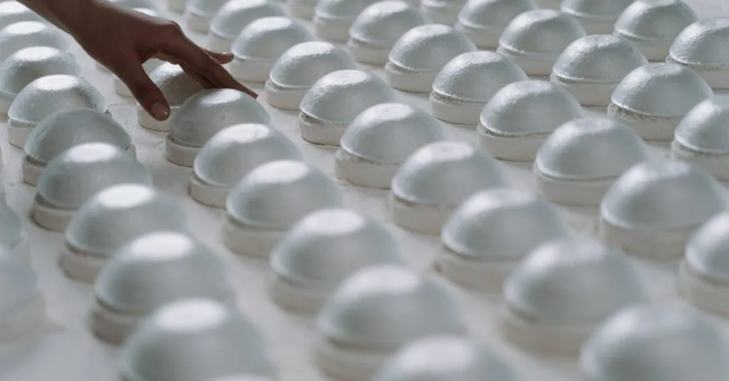 A person gently inspects rows of ceramic molds in a factory setting.