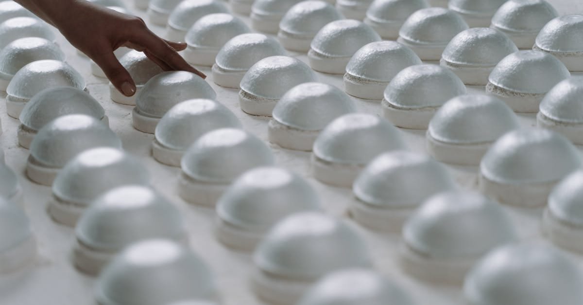 A person gently inspects rows of ceramic molds in a factory setting.
