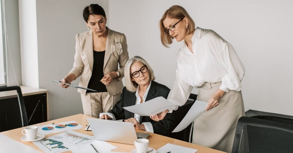 Three businesswomen discussing reports in a modern office environment.