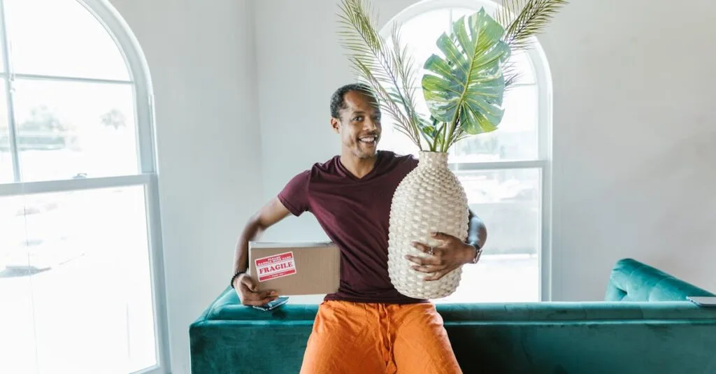 Smiling man holding a fragile box and plant during a home move.