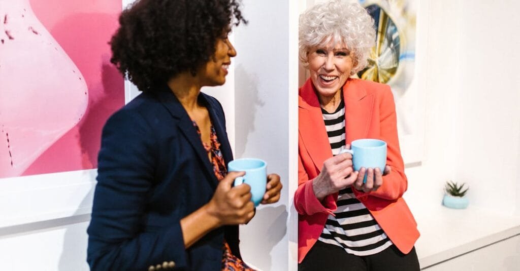Two women enjoying a coffee break in a modern and creative office setting, showcasing diversity and collaboration.