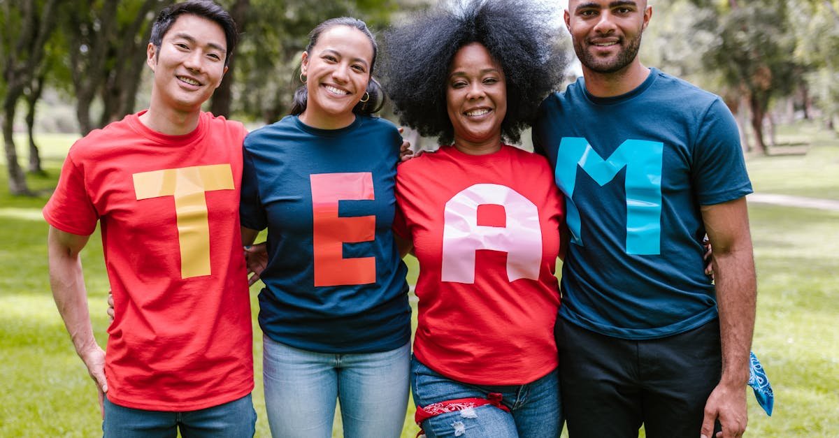 A diverse group of adults bonding and smiling in a park wearing TEAM shirts.