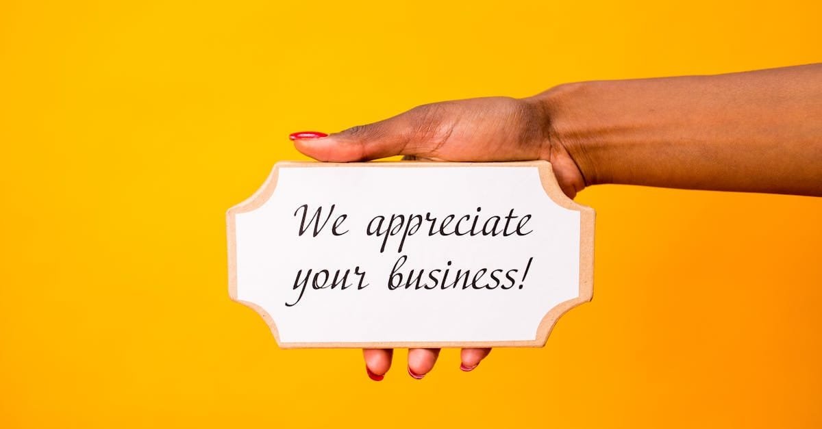 A hand holding a thank you sign with 'We appreciate your business!' on a vibrant yellow background.
