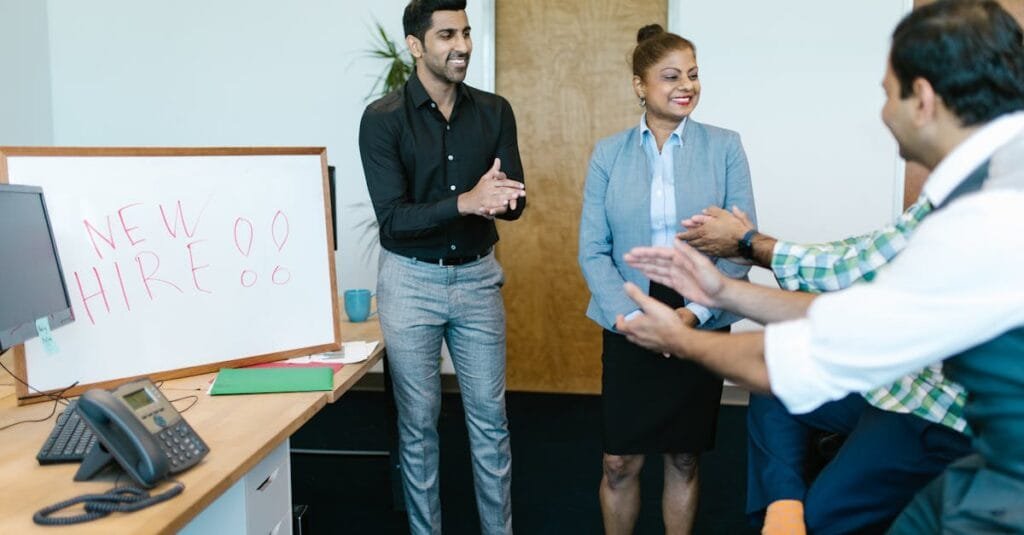 Colleagues joyfully applaud a new hire announcement in a modern office setting.