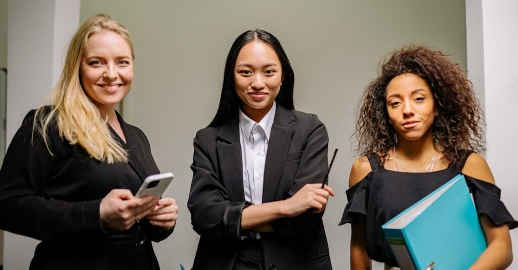 Three diverse women confidently posed in a modern office space.