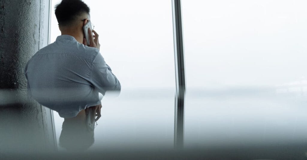 A professional making a phone call in a modern office setting with a city view.