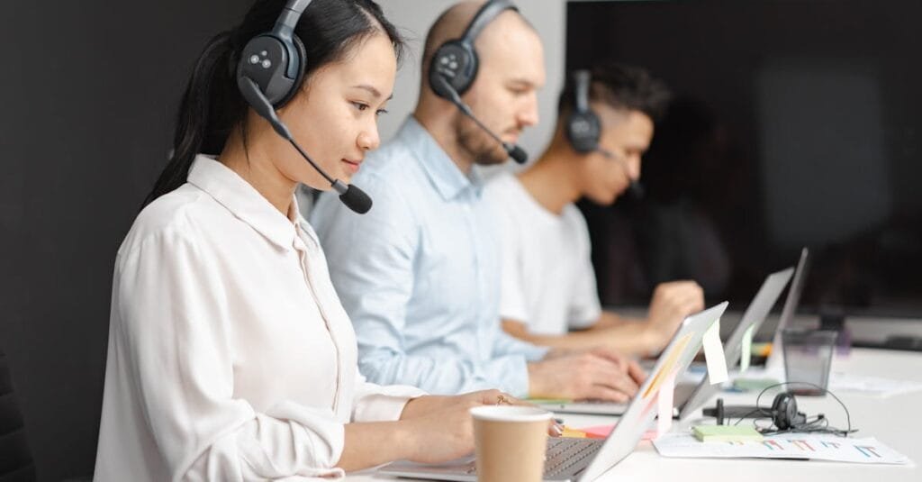 Customer service agents efficiently handle calls using laptops and headsets in a modern office.