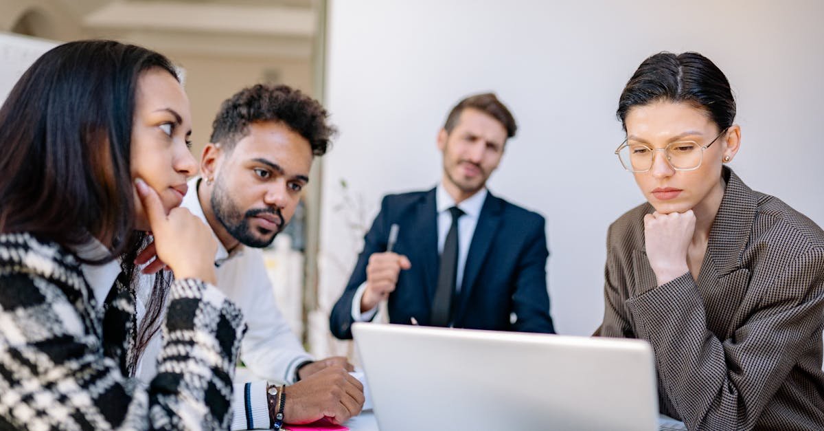 A diverse group of professionals working together around a laptop in a modern office setting.