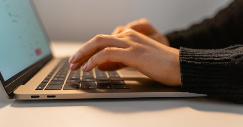 Close-up view of hands typing on a laptop keyboard, illustrating the concept of remote work and technology.