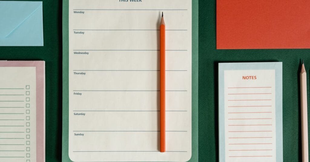 Flat lay of weekly planner, notes, envelopes, and pencils on a green background representing organization.
