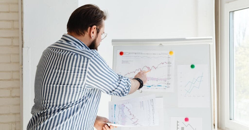 A businessman pointing at financial charts on a whiteboard, discussing stock market trends.