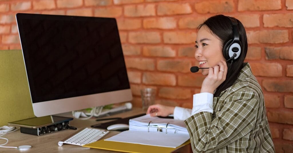 Smiling female call center agent working at desk with computer and headset.