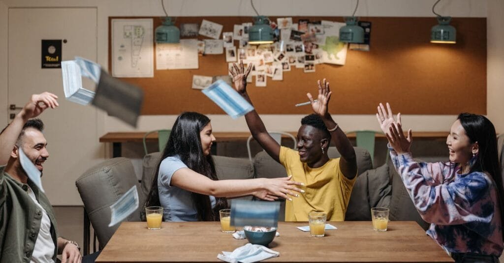 Group of diverse friends celebrating indoors, throwing masks, and enjoying drinks.