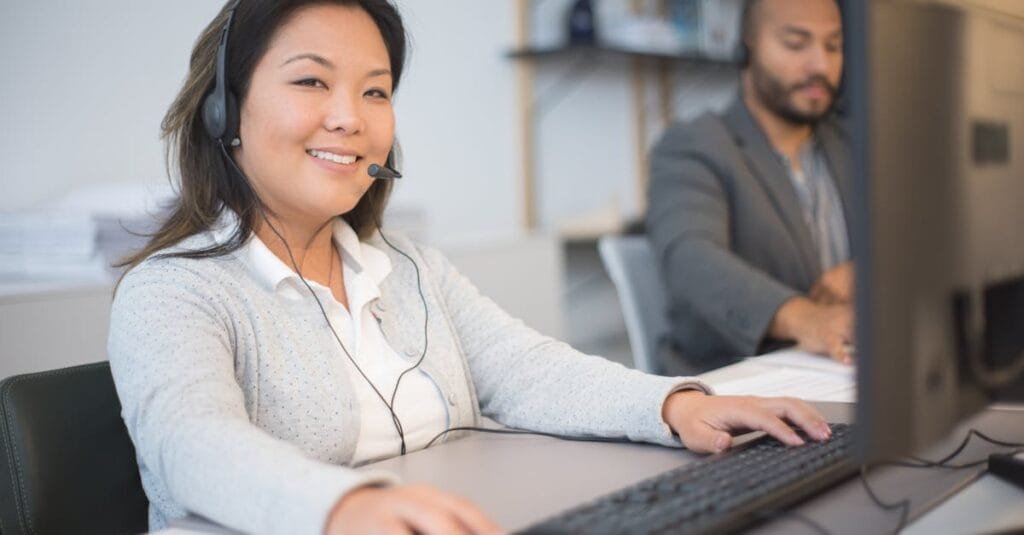 Two call center employees working with headsets in a modern office setting.