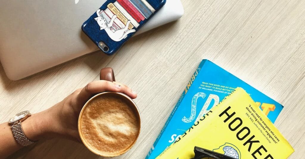 Overhead view of a workspace featuring books, coffee, and a smartphone on a wooden table.