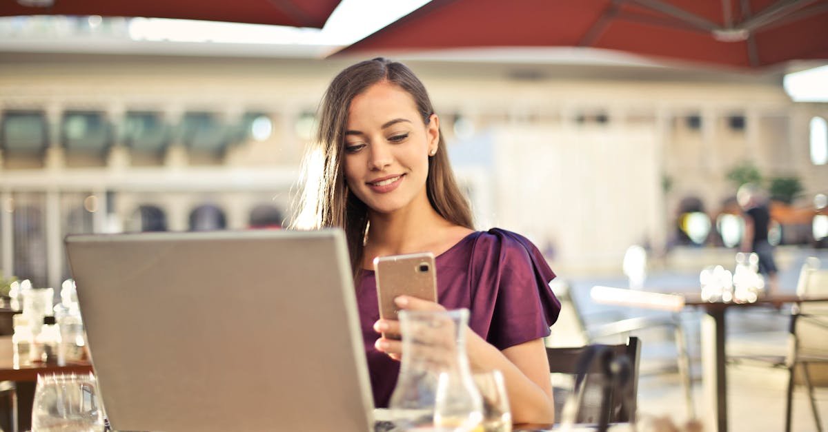 Woman enjoying remote work at a café, using a laptop and smartphone.