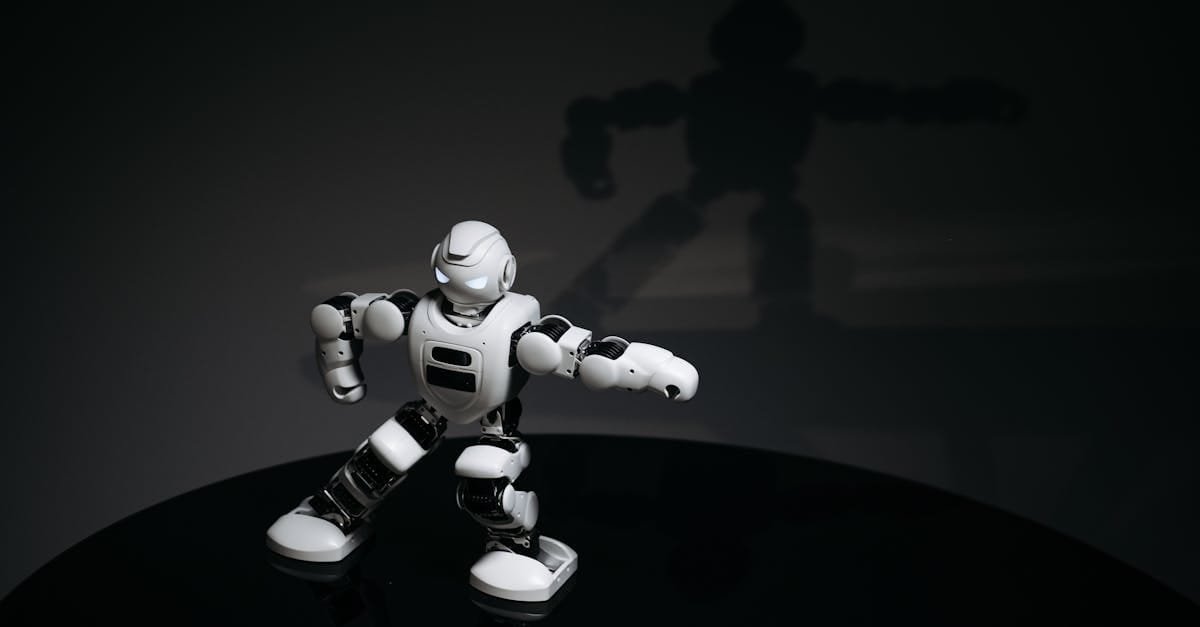 A futuristic white toy robot striking a pose in a dimly lit studio with a shadow cast behind it.