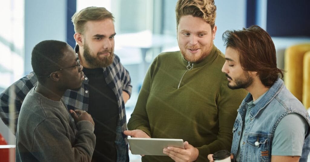 A group of four men engaging with a digital tablet in an indoor meeting setting.
