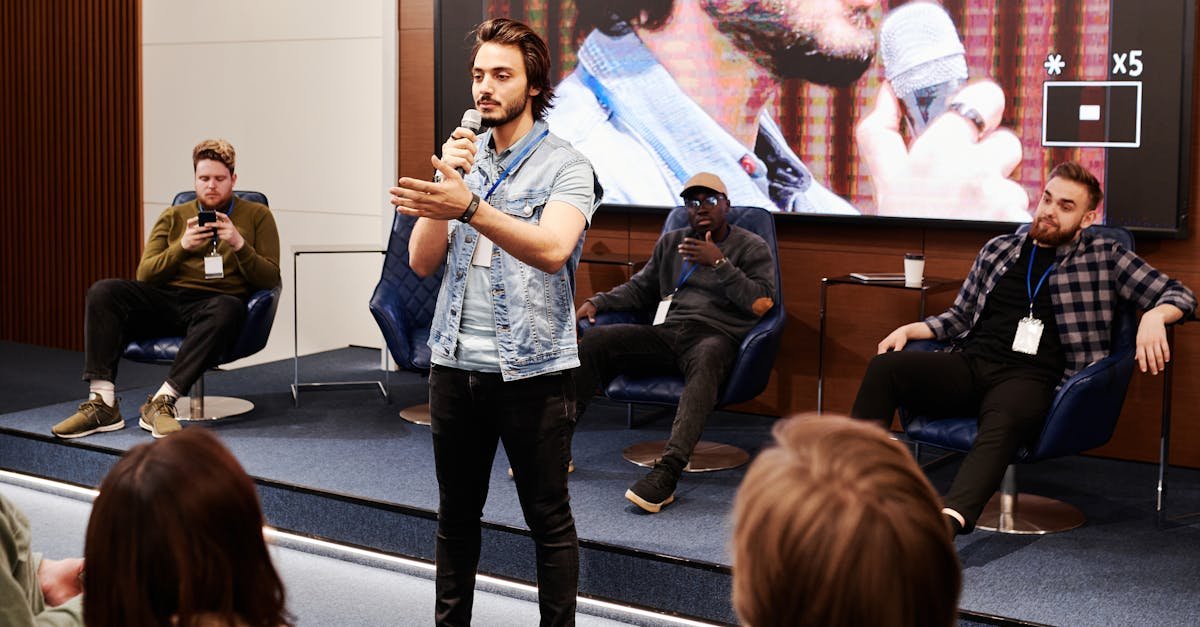 Speaker holds microphone, engaging audience at an indoor business conference with a panel in the background.