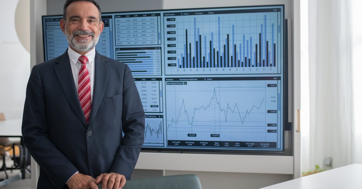 Smiling businessman in office analyzing financial graphs on a large screen, demonstrating professional success.