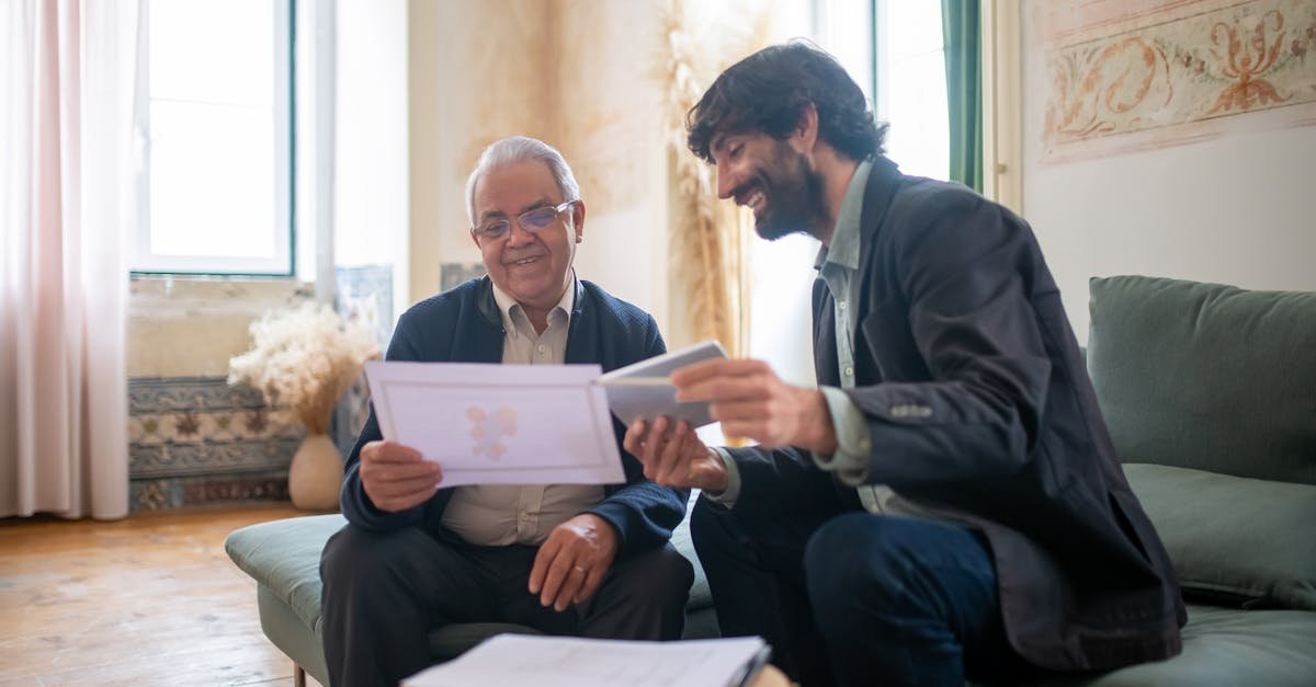 An elderly man and a younger man in a casual office setting, discussing documents with smiles.
