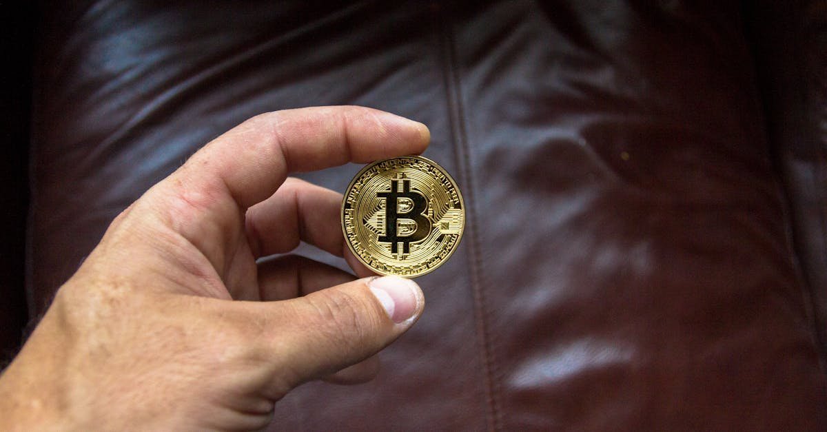 Close-up of a hand holding a gold Bitcoin cryptocurrency coin on a leather background.