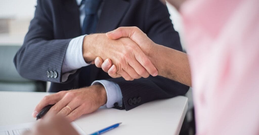 Two businessmen shaking hands across table, symbolizing agreement and partnership in an office environment.