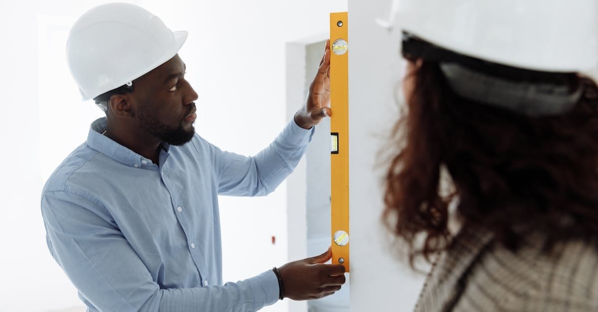 An adult man in safety gear uses a spirit level indoors for accurate measurements.