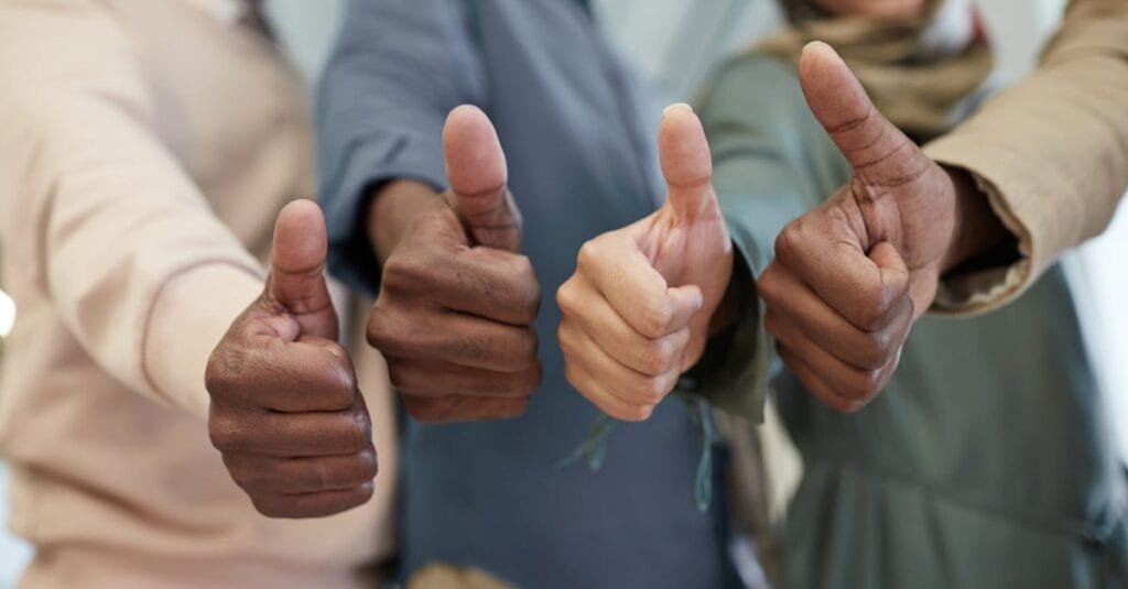 Close-up of a diverse team giving thumbs up indoors, symbolizing success and unity.