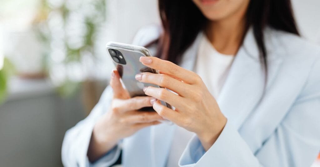 A woman with manicured nails uses a smartphone inside a modern setting.