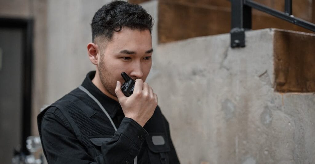 Asian security guard using walkie talkie in an indoor setting, demonstrating communication and alertness.