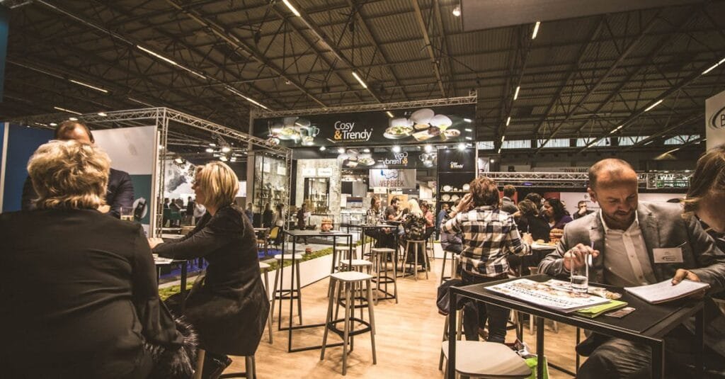 A bustling indoor business expo with professionals networking and engaging at various booths.