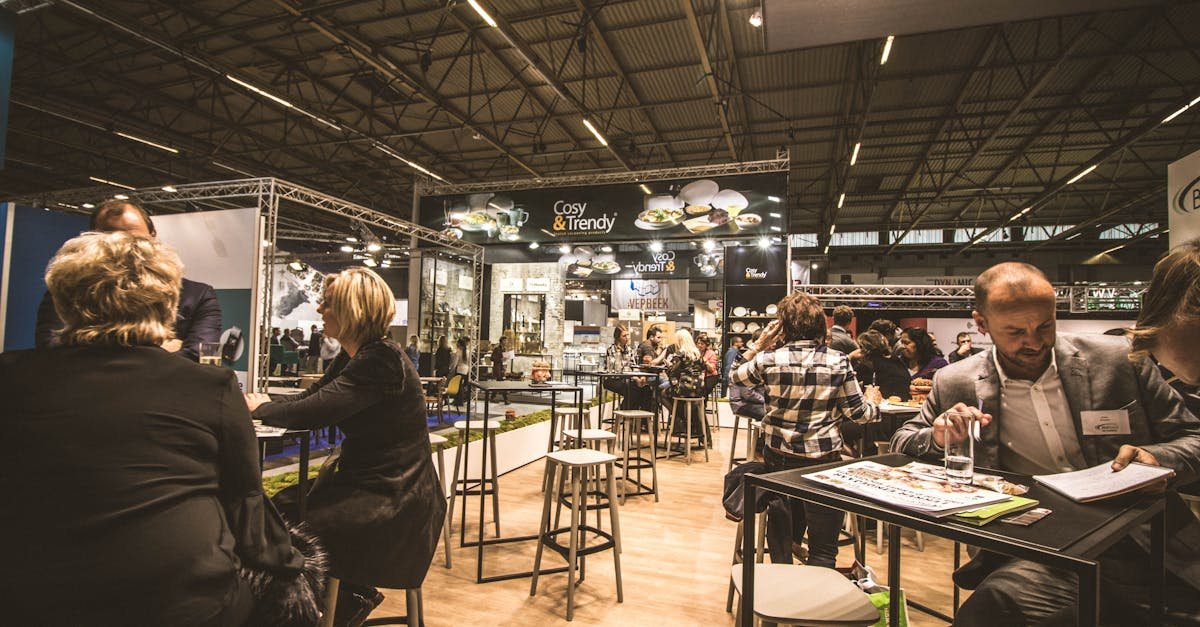 A bustling indoor business expo with professionals networking and engaging at various booths.