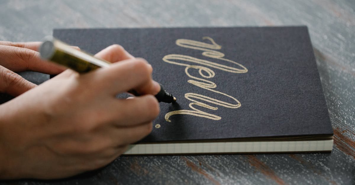 Close-up of a person writing elegant calligraphy on a black notebook using a golden pen.