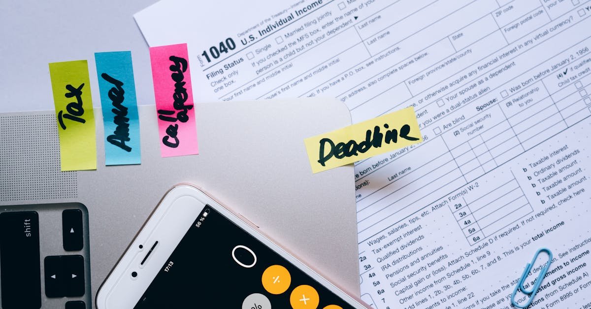 Office desk flat lay showing tax documents, calculator app on smartphone, sticky notes, and paperclips.