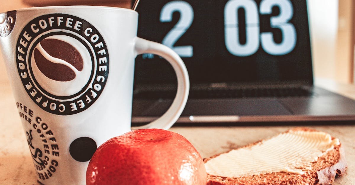 A cozy breakfast setup with coffee, bread, and fruit next to a laptop.