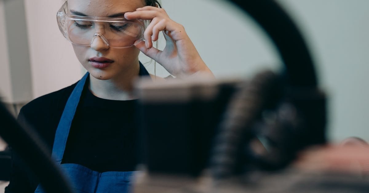 Young woman wearing safety glasses and apron in an industrial setting, focusing on her task.