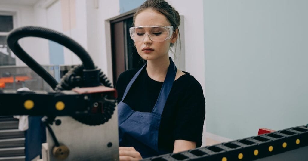 A female engineer operates machinery with precision in an industrial setting, wearing safety glasses.