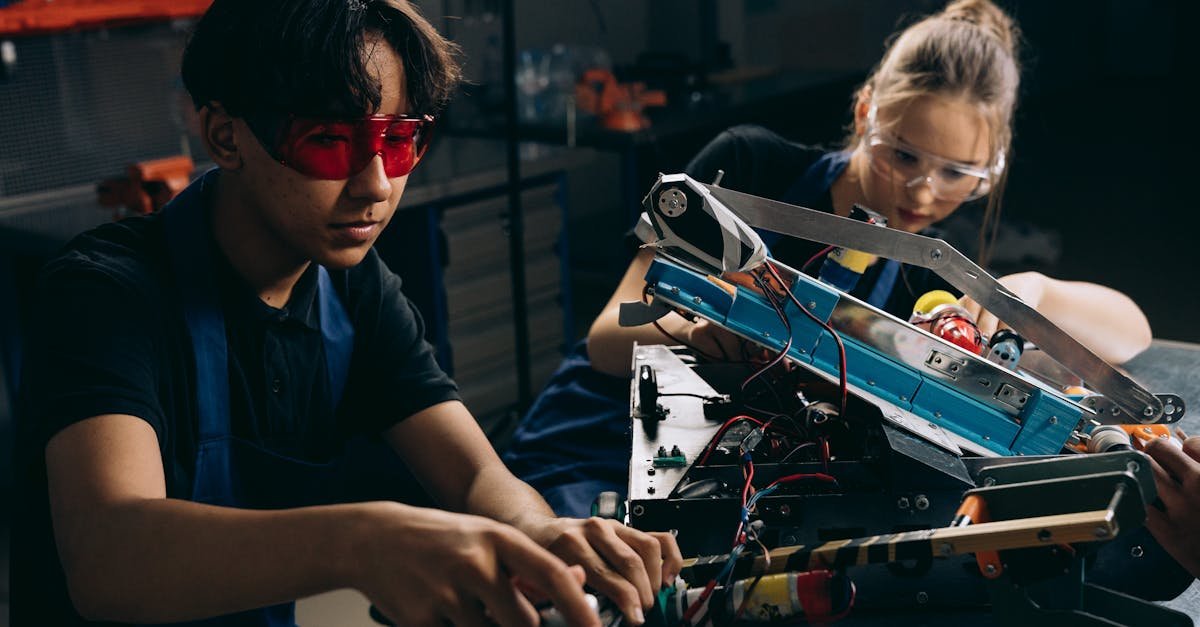 Two young engineers working on robotic equipment in a workshop setting.
