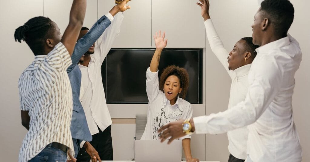 Group of diverse professionals raising hands during a collaborative team meeting in a modern office.