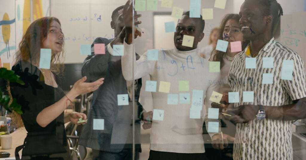 A diverse group of colleagues collaborates using sticky notes on a glass wall in an office.