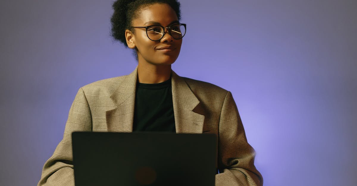 Portrait of a confident woman in a blazer working on a laptop, looking away thoughtfully in a studio setting.
