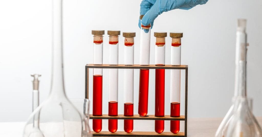 Close-up of gloved hand handling test tubes in a scientific laboratory setting.