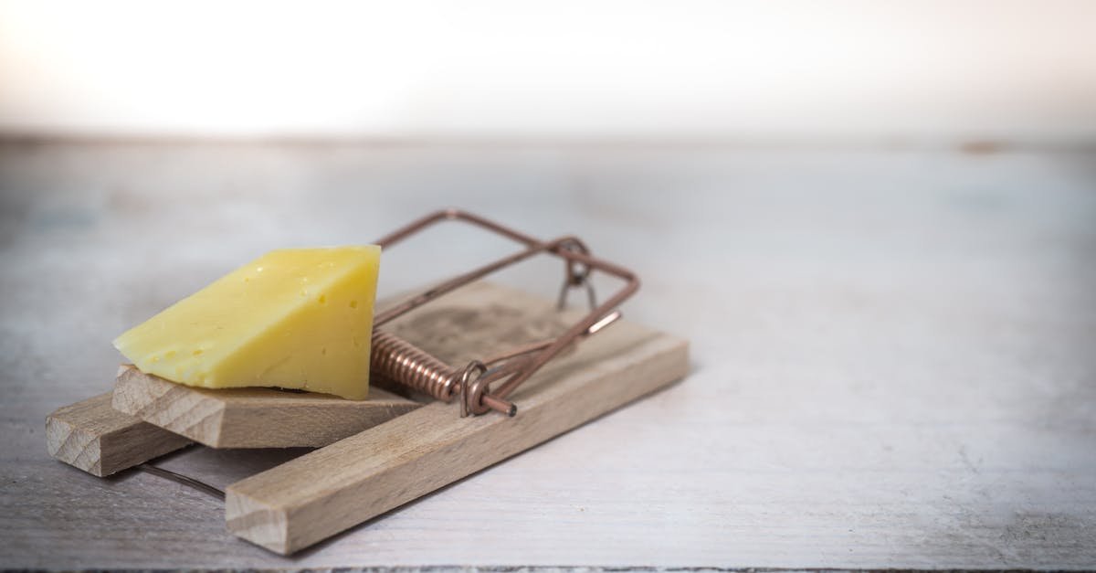 Close-up of a wooden mousetrap with a piece of cheese on a rustic table surface.