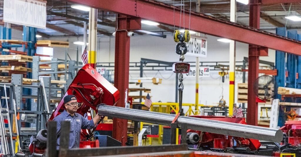 Worker operating heavy machinery in a factory, moving steel bars. Industrial scene indoors.