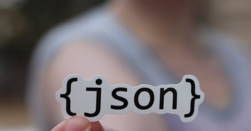A hand holding a JSON text sticker, symbolic for software development.